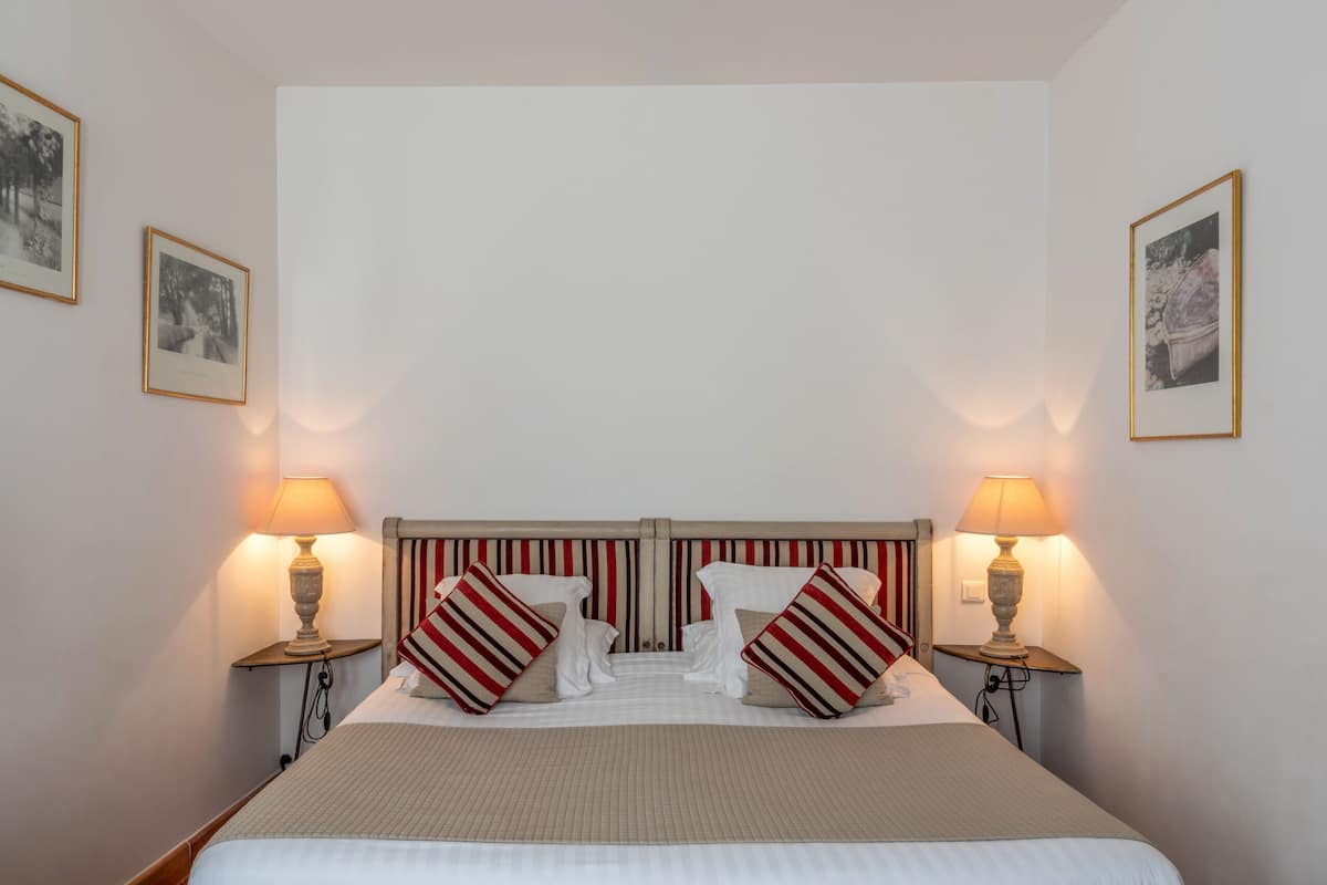 A neatly made bed with striped pillows, two bedside lamps, and framed pictures on the walls.