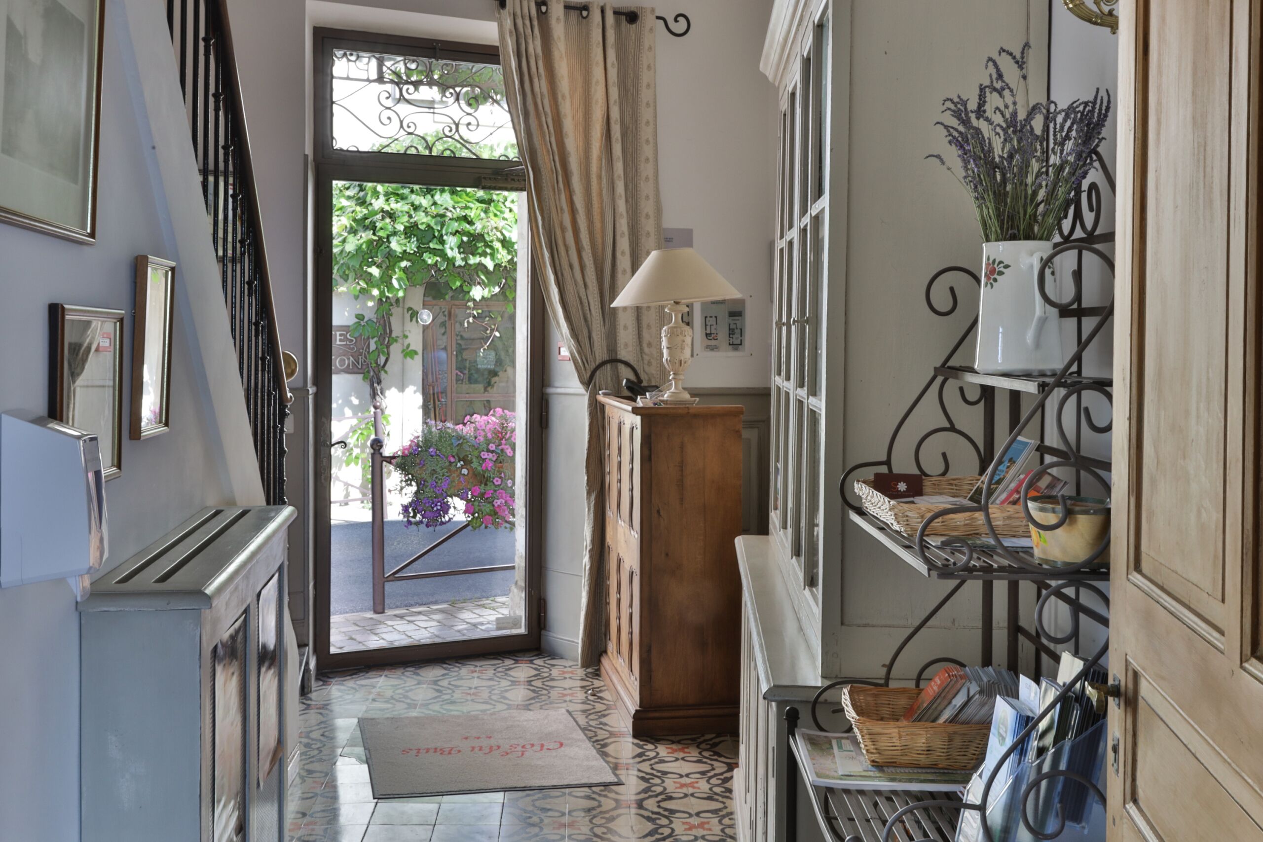 A hallway with a staircase, a door leading outside, a lamp, and shelves with books and decorative items.