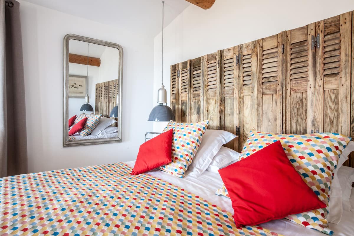 A bedroom with a bed, pillows, a mirror, and a wooden headboard.