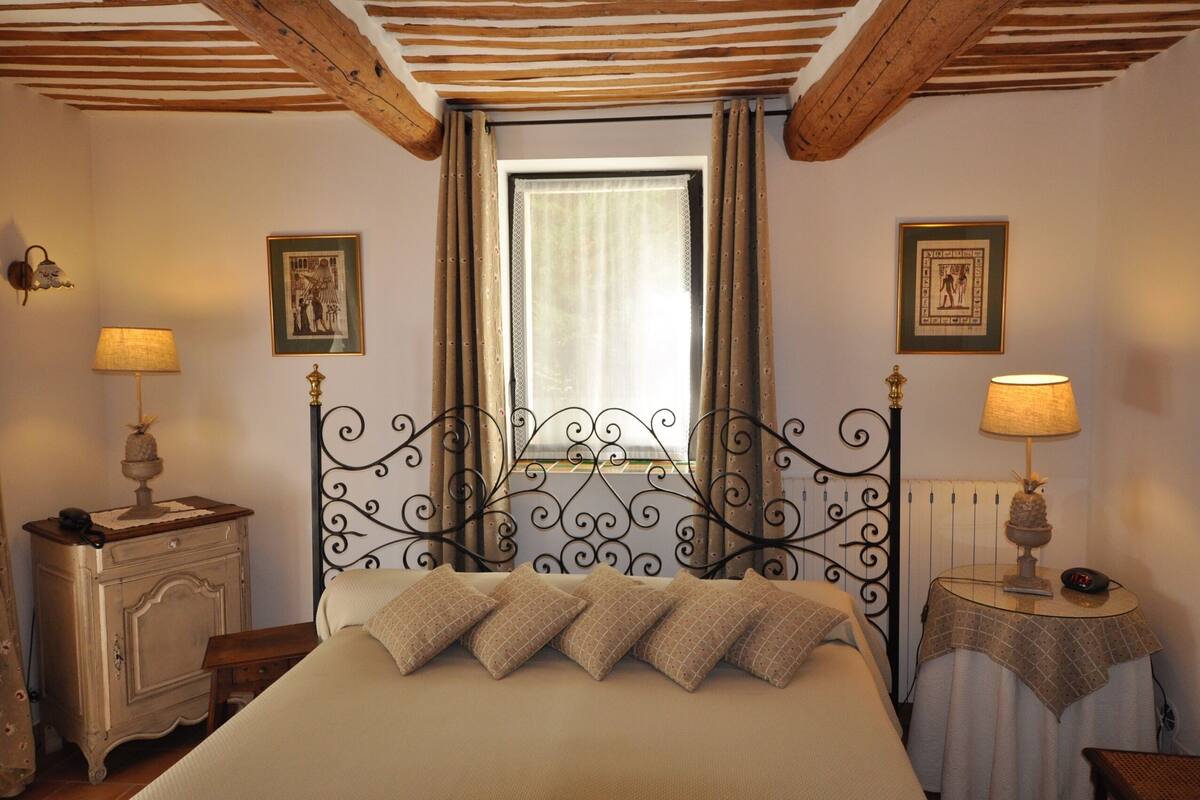 A bedroom with a bed, two bedside tables, a window with curtains, and wall-mounted lamps.