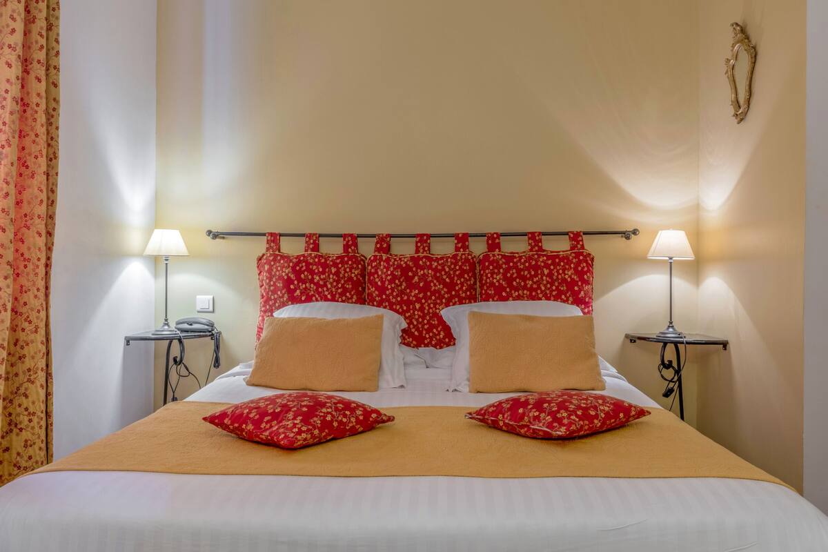 A hotel room with a bed, two bedside lamps, a telephone, and a wall-mounted light fixture.