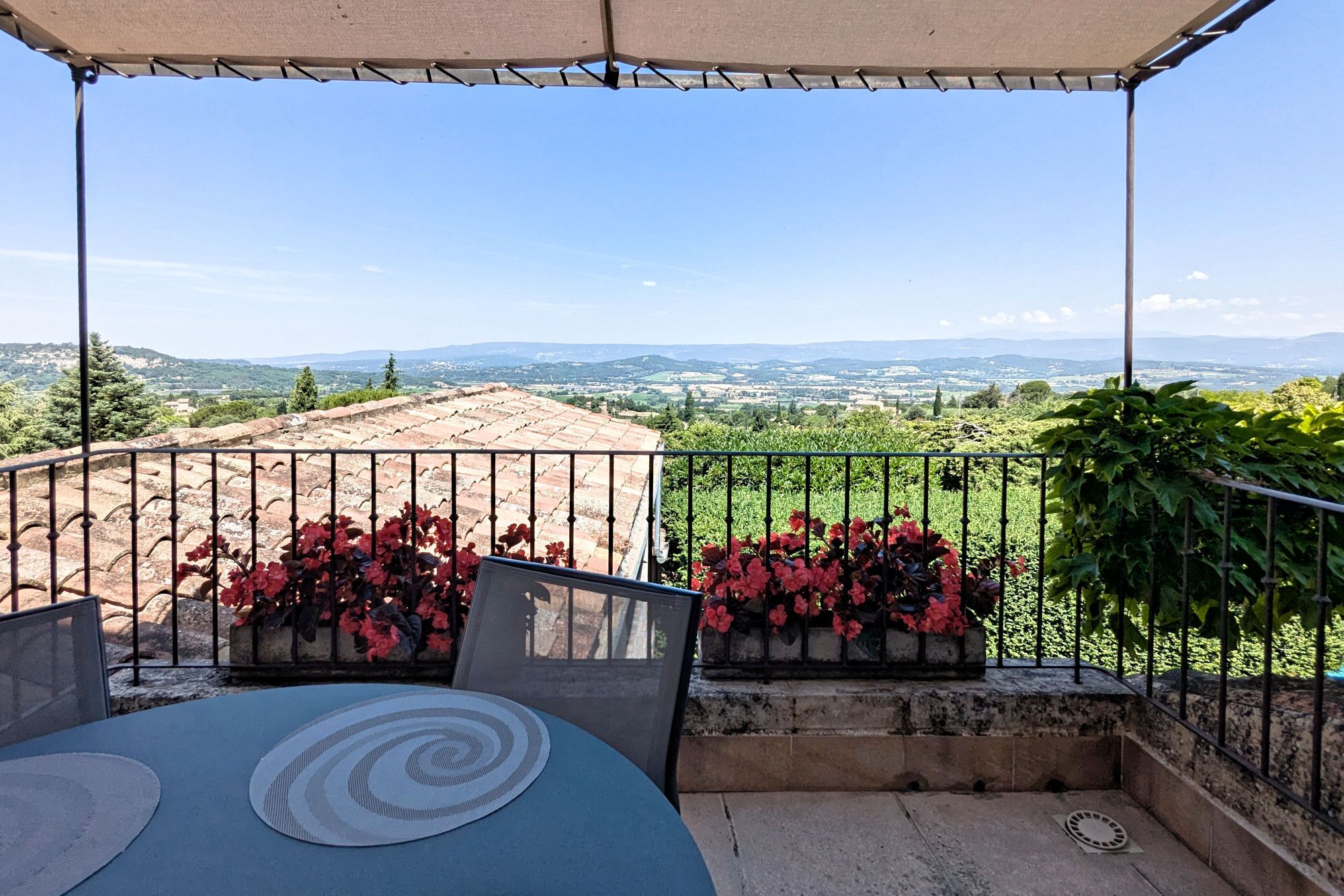 A terrace with a view of a rural landscape, featuring a table with a circular mat and red flowers.
