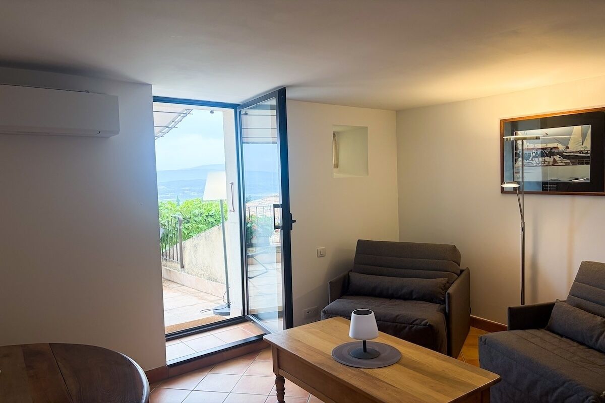 Un salón con sofá, una mesa con lámpara, un cuadro enmarcado en la pared y una puerta corrediza de vidrio que da a un área exterior.