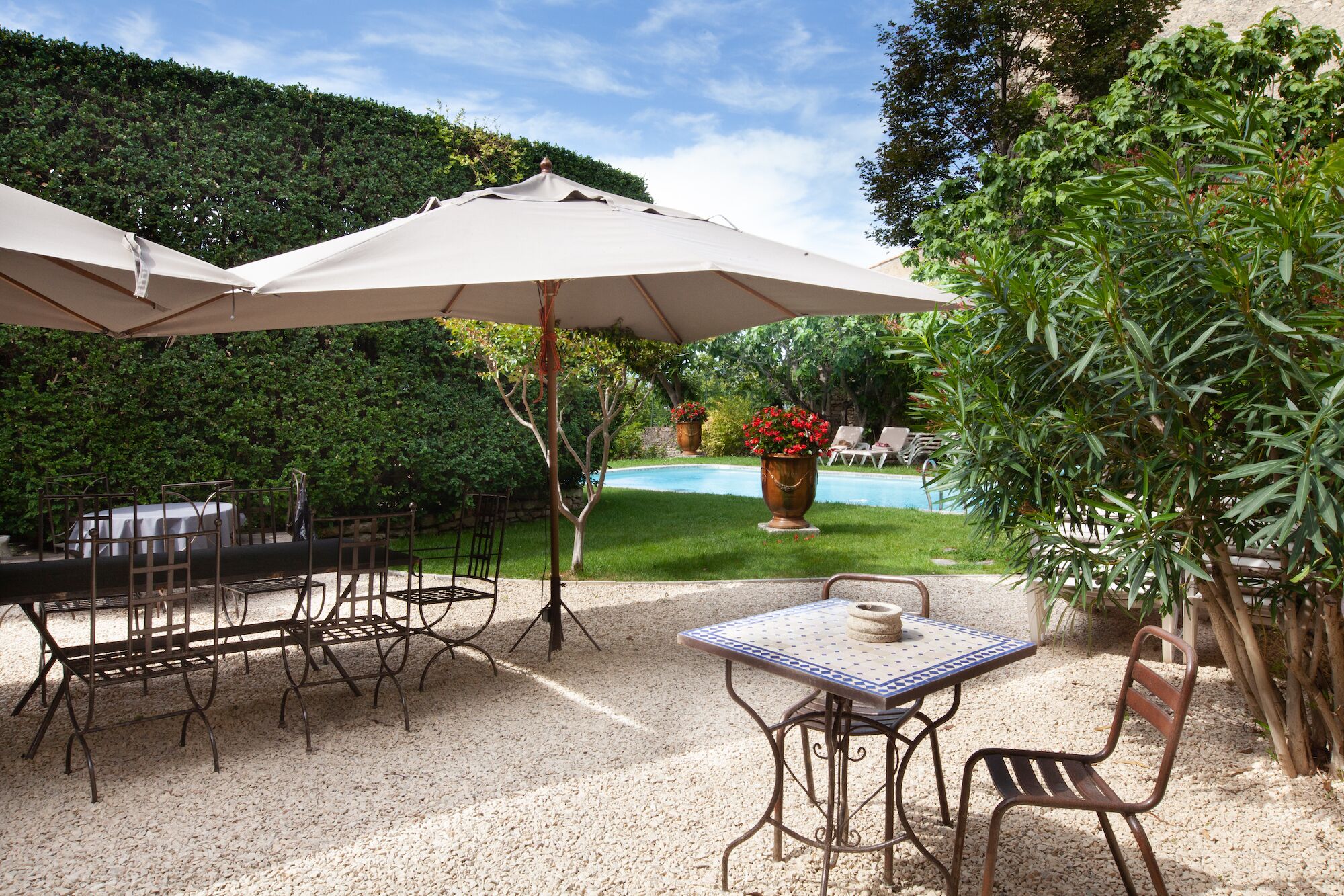 Un patio al aire libre con piscina, rodeado de follaje y amueblado con sillas y mesas de metal.