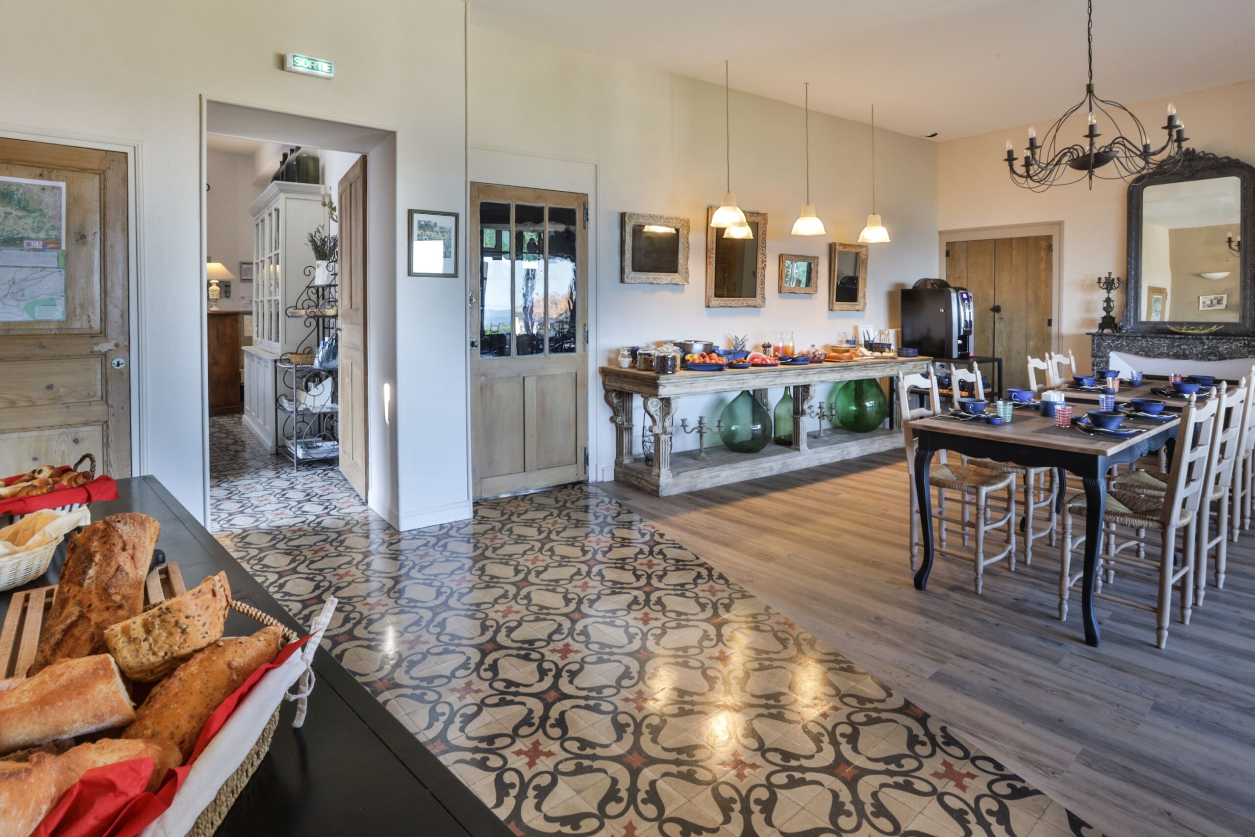 A kitchen with a wooden floor, a dining table with chairs, a chandelier, and a large mirror.