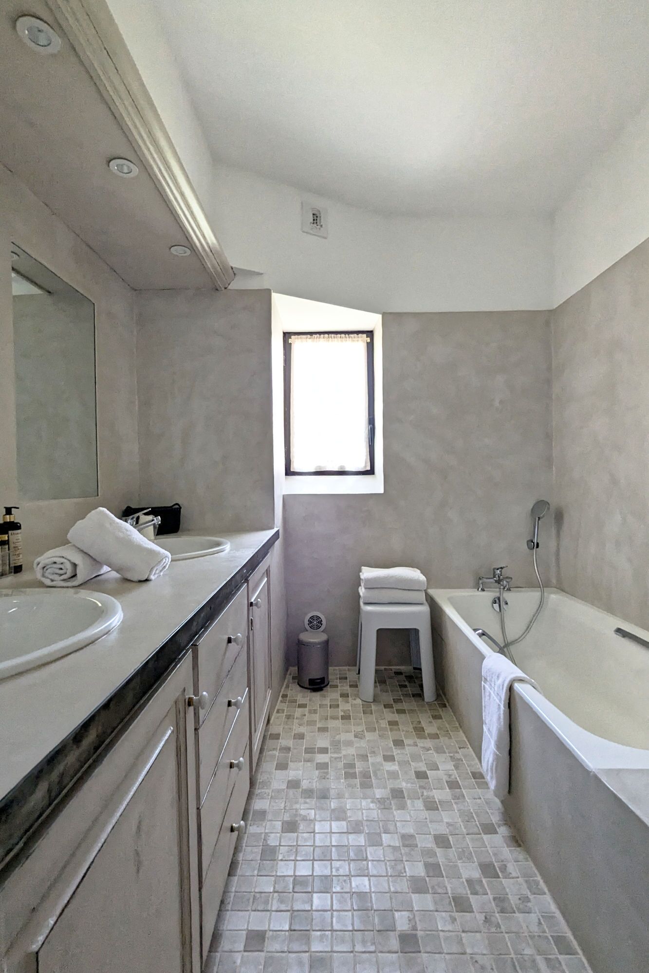 A modern bathroom with a large vanity, a bathtub, and a window providing natural light.