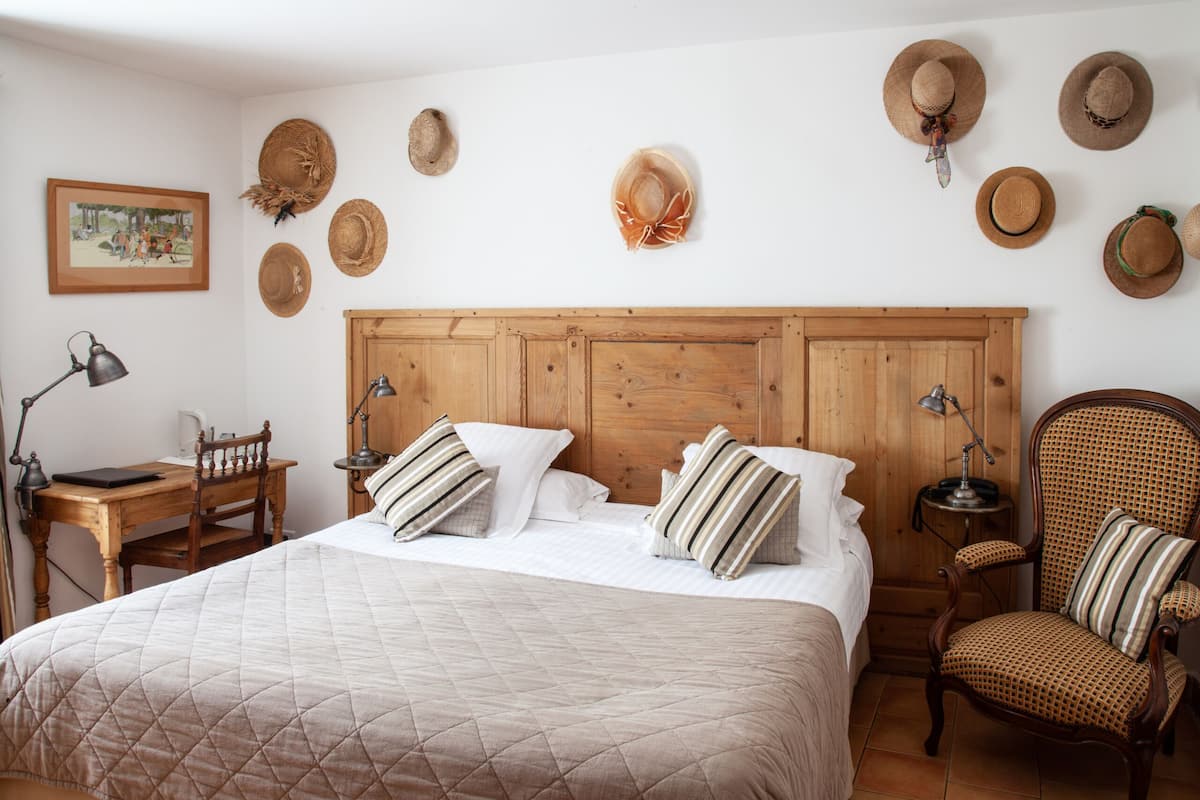 A bedroom with a wooden headboard, a bed with striped pillows, a desk with a lamp, and a chair.
