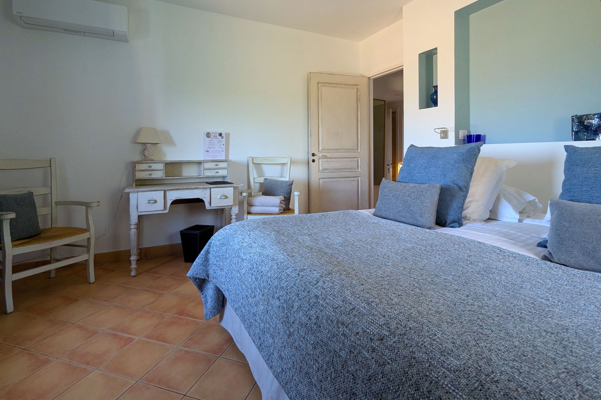 A bedroom with a bed, a desk, a chair, and a door.