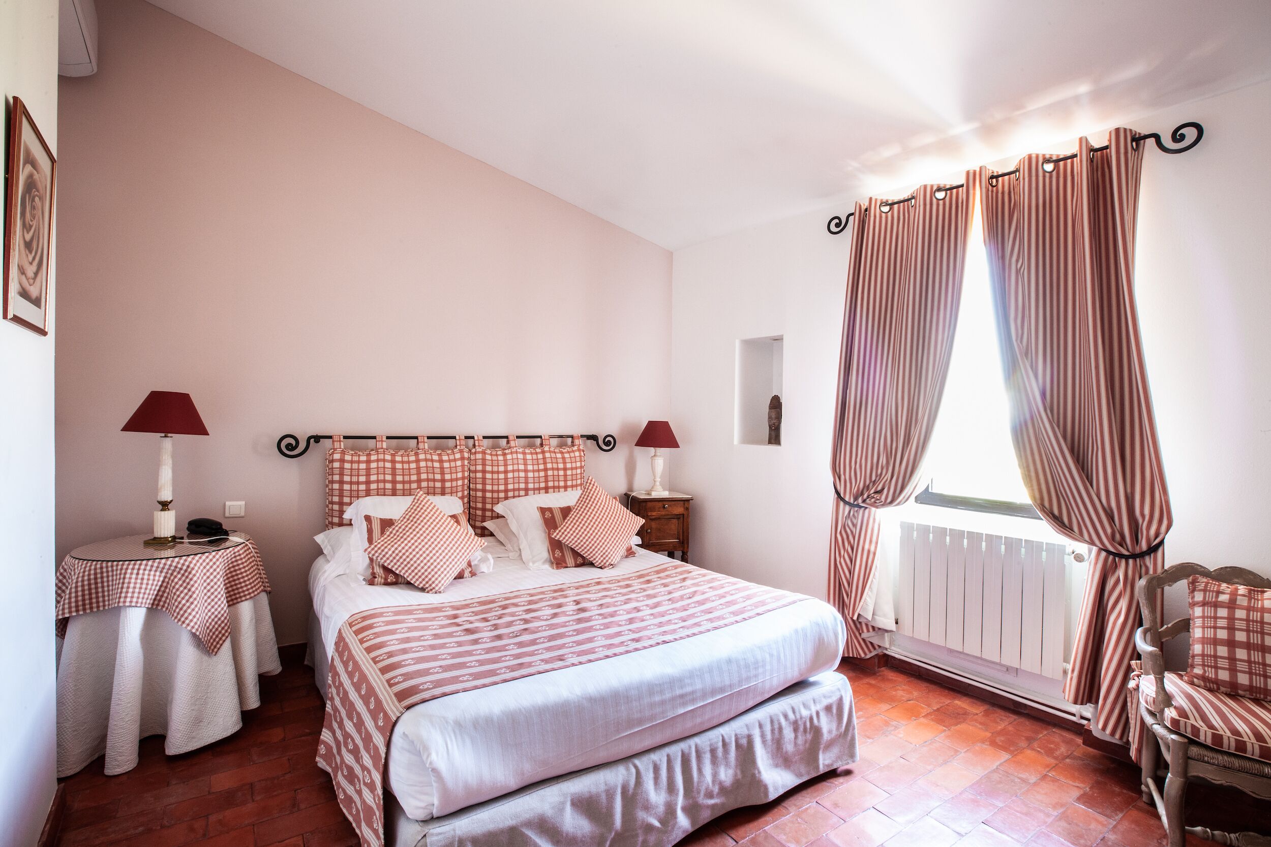 Une chambre bien rangée, avec un lit, deux tables de chevet, une chaise et une fenêtre avec des rideaux.