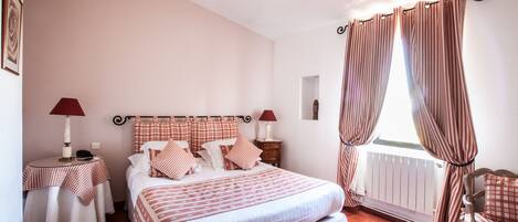 A neatly arranged bedroom with a bed, two bedside tables, a chair, and a window with curtains.