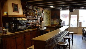 Un bar avec des comptoirs et des tabourets en bois, une machine à café et des étagères remplies de bouteilles et de verres.