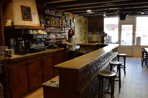 A bar with wooden counters and stools, a coffee machine, and shelves with bottles and glasses.
