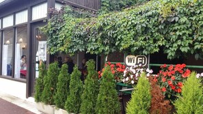 A building with a 'WiFi' sign, potted plants, and a window with a person inside. - A La Vieille Halle (Souppes-sur-Loing)
