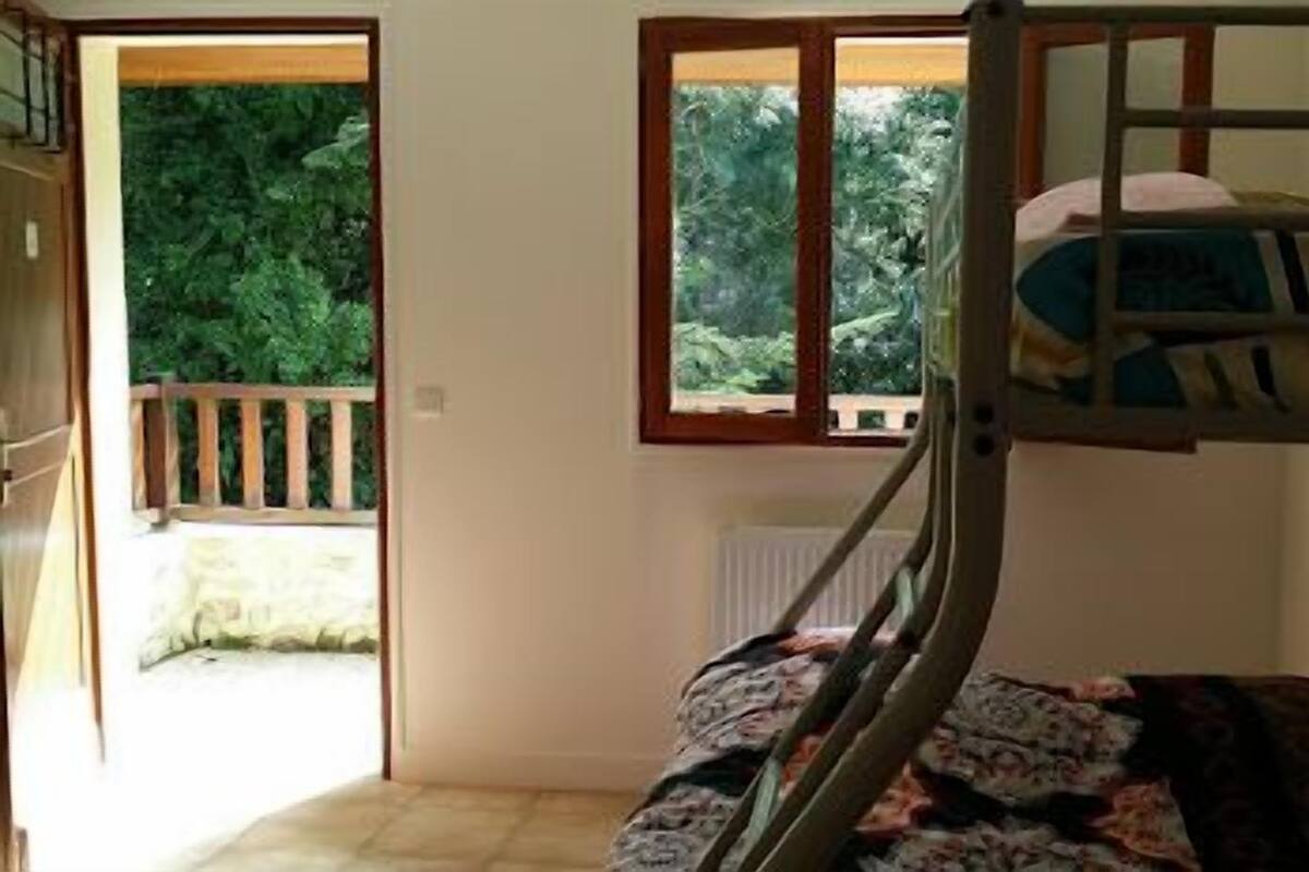 A bunk bed room with a window, a door leading outside, and a view of greenery.