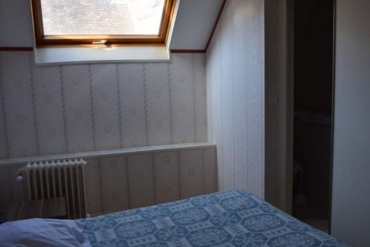 A small, dimly lit room with a single bed, a radiator, and a window with a view of the outside.