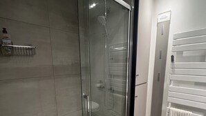 Un baño moderno con ducha envuelta en vidrio, un toallero blanco y un inodoro a la vista.