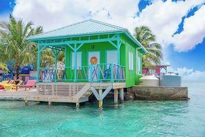 A turquoise and green structure with a balcony, located on a pier over clear turquoise water.