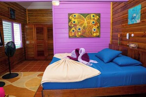 A room with a bed, a fan, a window with blinds, and a painting on the wall.