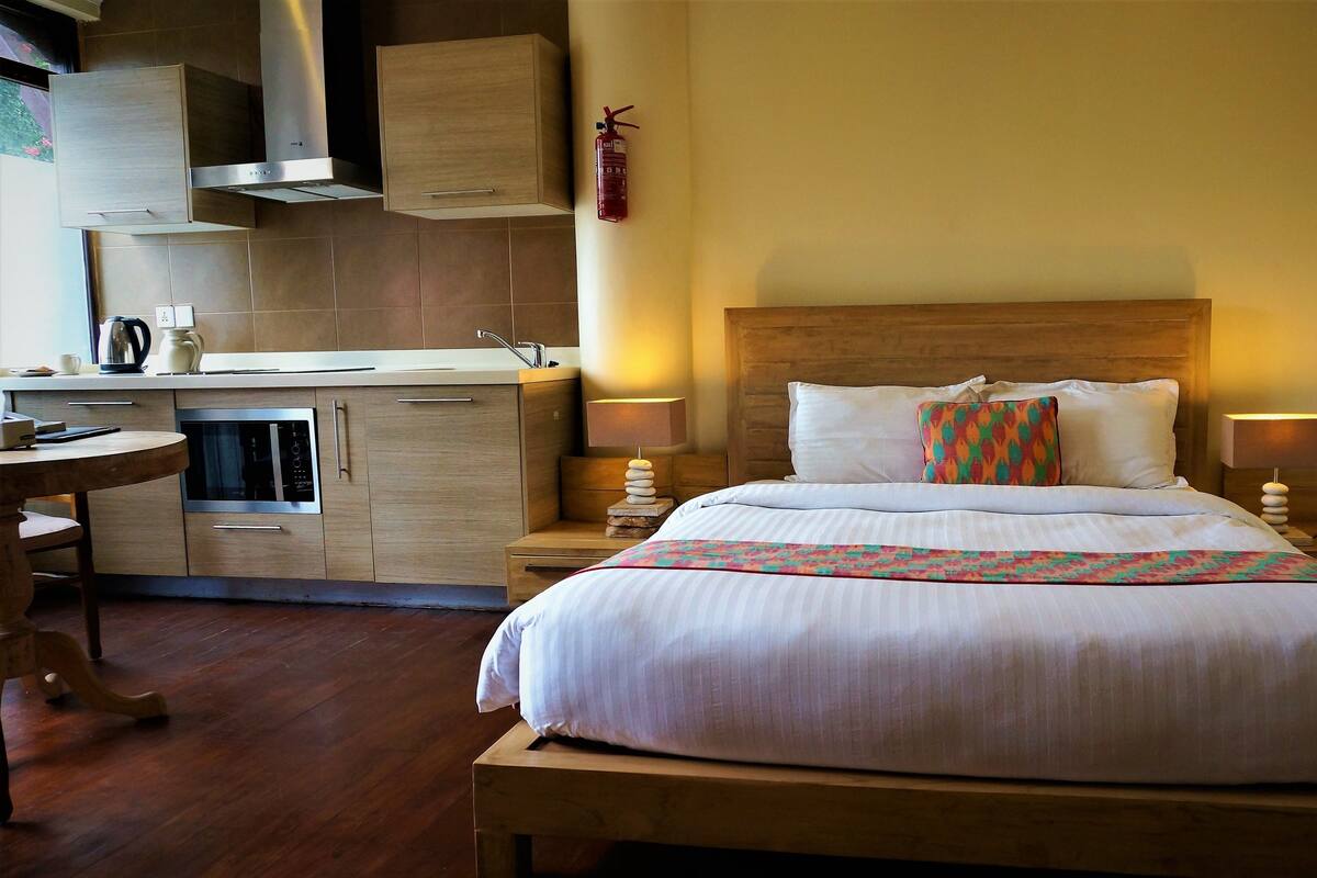 A hotel room with a bed, bedside tables, a small kitchenette, and a wooden headboard.