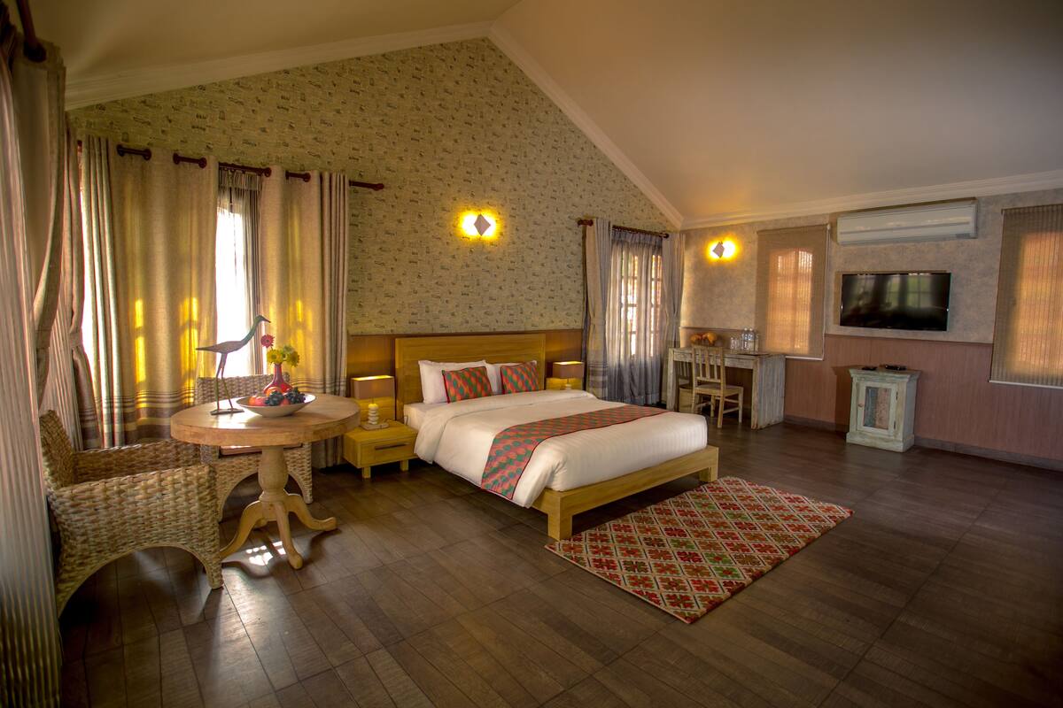 A hotel room with a bed, bedside tables, a TV, a small table with a vase, and a chair.