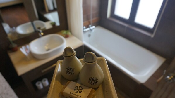 A bathroom with a sink, mirror, and bathtub. There are two bottles with flower designs and a bar of soap. - Tangalwood Boutique Hotel (Kathmandu)