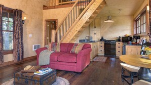 Un salón espacioso con una escalera de madera que sube a un nivel superior, un sofá rojo acogedor y una mesa de comedor de madera.