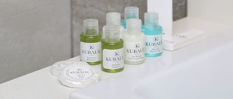 Una encimera de baño con diversos artículos de aseo KUBALIC para hotel, como champú, acondicionador y gel de ducha.