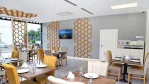A modern dining area with hexagonal wall decor, wooden tables, and yellow chairs. - Kubalic Hotel (Ordu)