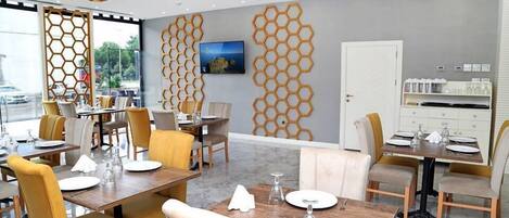 A modern dining area with hexagonal wall decor, wooden tables, and yellow chairs.