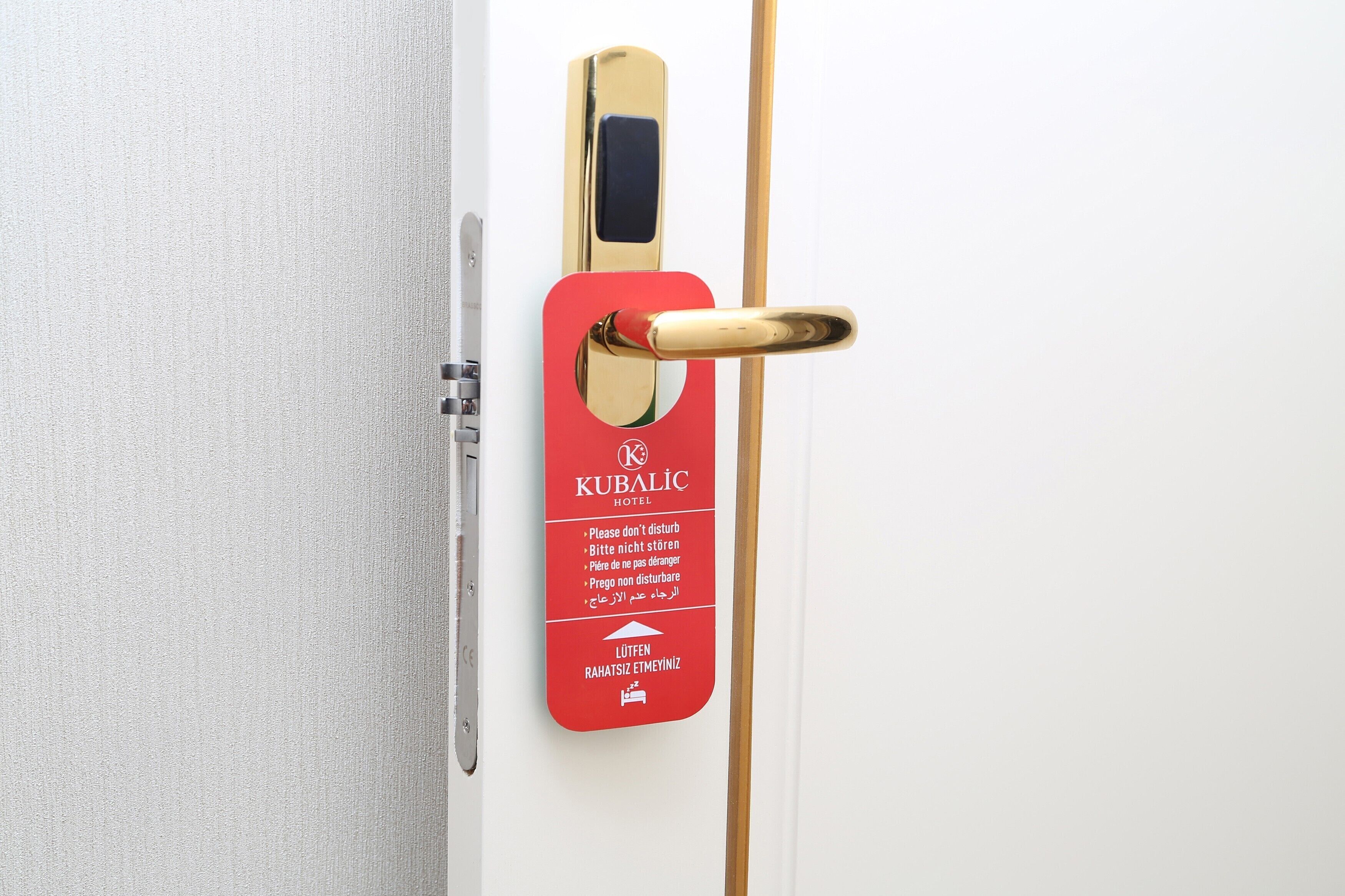 Een hoteldeur met een rood bord waarop meertalige instructies en de naam van het hotel staan.