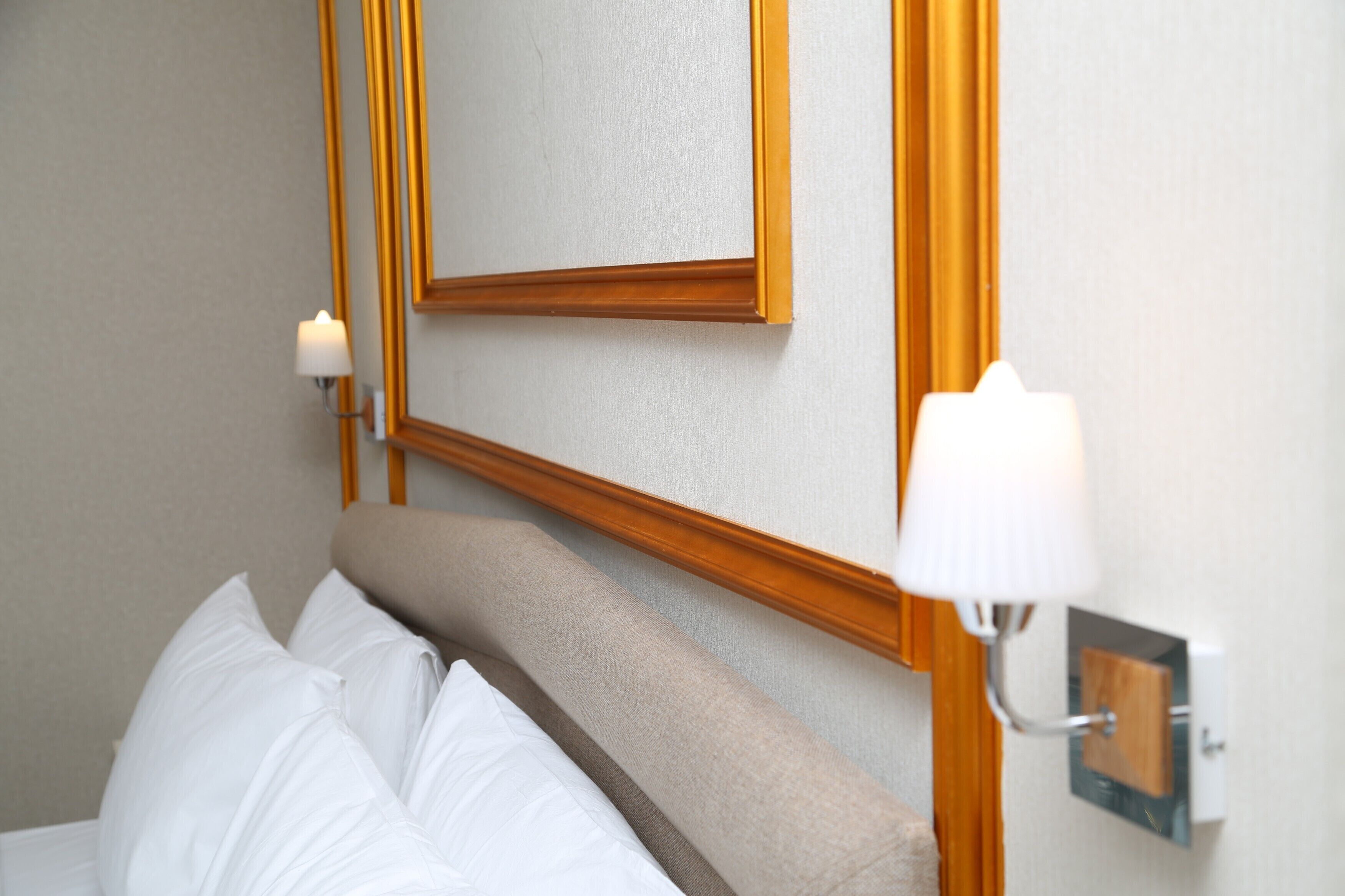 A hotel room with a bed, a wall-mounted mirror, and two wall sconces.