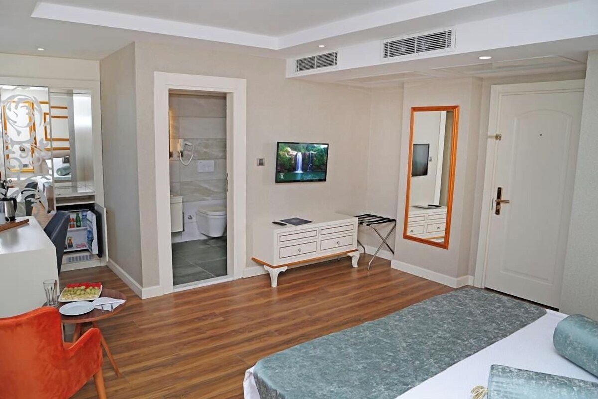 A bedroom with a bed, a TV, a dresser, and a bathroom visible through an open door.