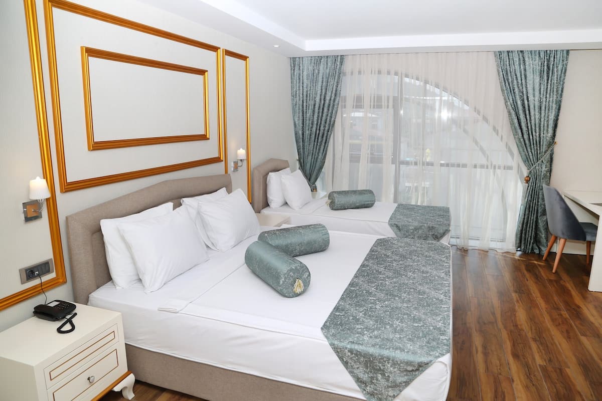 A hotel room with a large bed, a desk, and a view of a building through sheer curtains.
