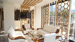 A modern living room with white sofas and a glass coffee table, wooden accents, and a large TV. - Kubalic Hotel (Ordu)