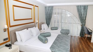 A hotel room with a large bed, a desk, and a view of a building through sheer curtains. - Kubalic Hotel (Ordu)
