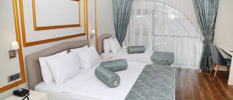 A hotel room with a large bed, a desk, and a view of a building through sheer curtains.