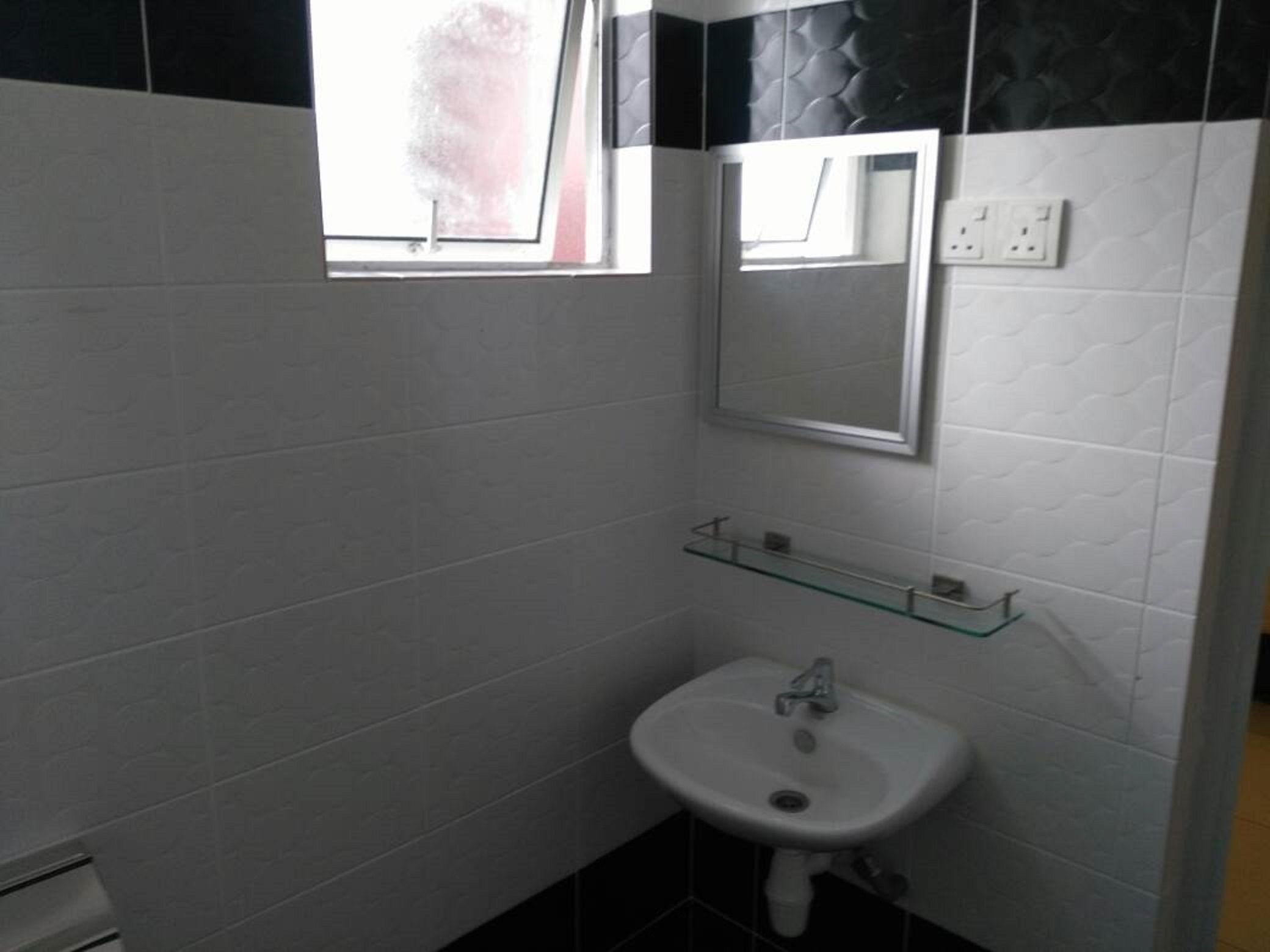 A small bathroom with white tiled walls, a white sink, and a mirror above it. There is a window with a view of the outside.