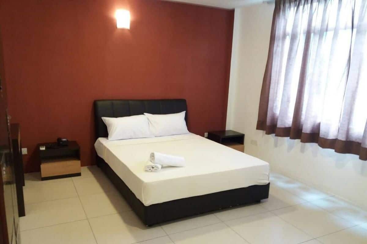 Une chambre d’hôtel avec un lit, des tables de chevet, une petite table et une fenêtre avec des rideaux.