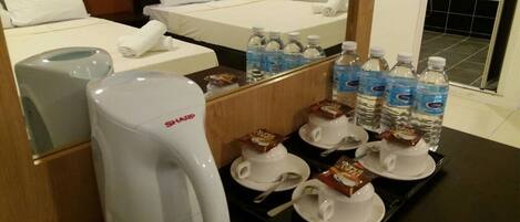 Habitación de hotel con dos camas, cafetera, botellas de agua y alimentos para el desayuno sobre una bandeja.