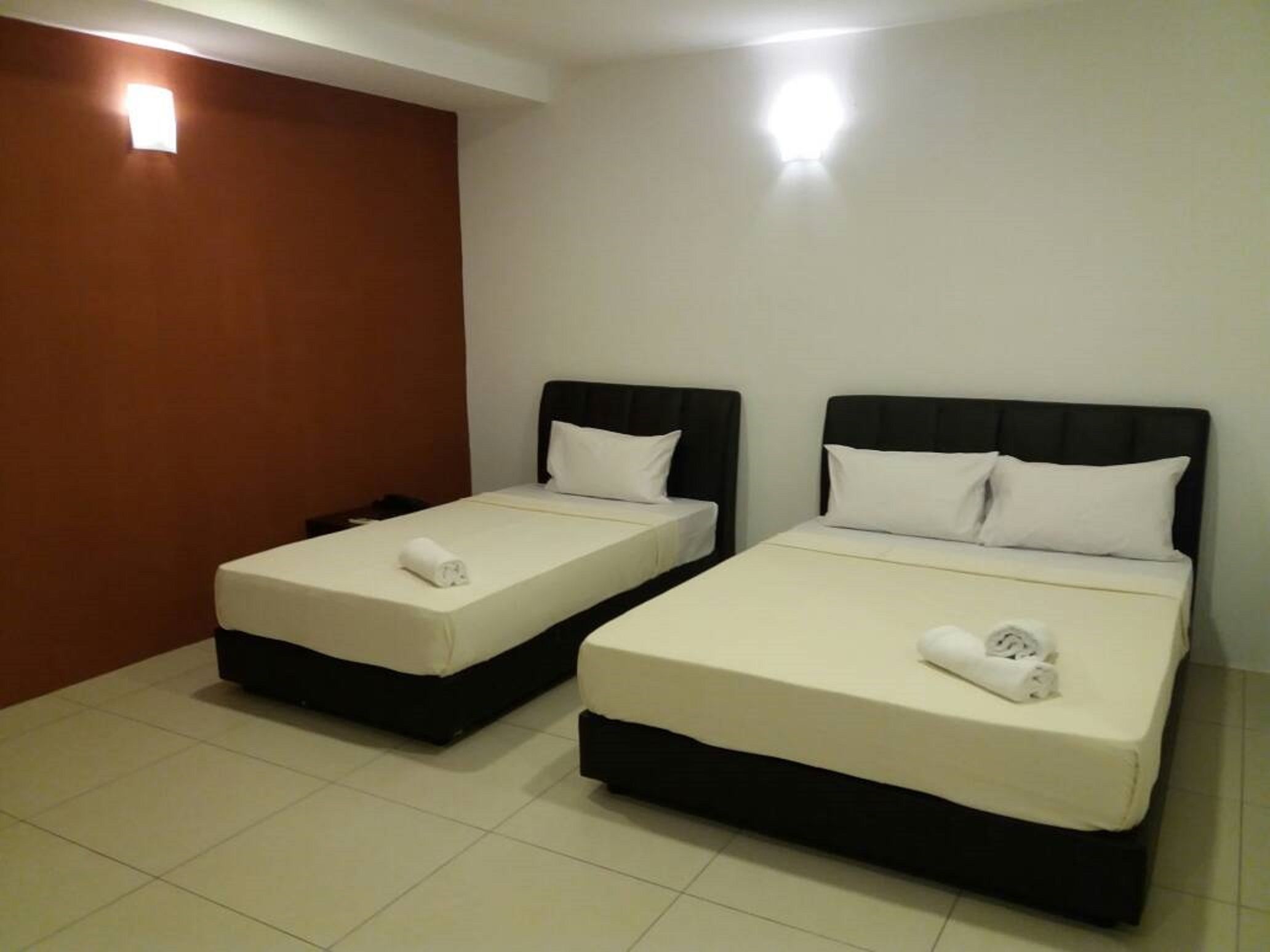 Una habitación de hotel con dos camas individuales, cada una con cabecera negra y ropa de cama blanca.