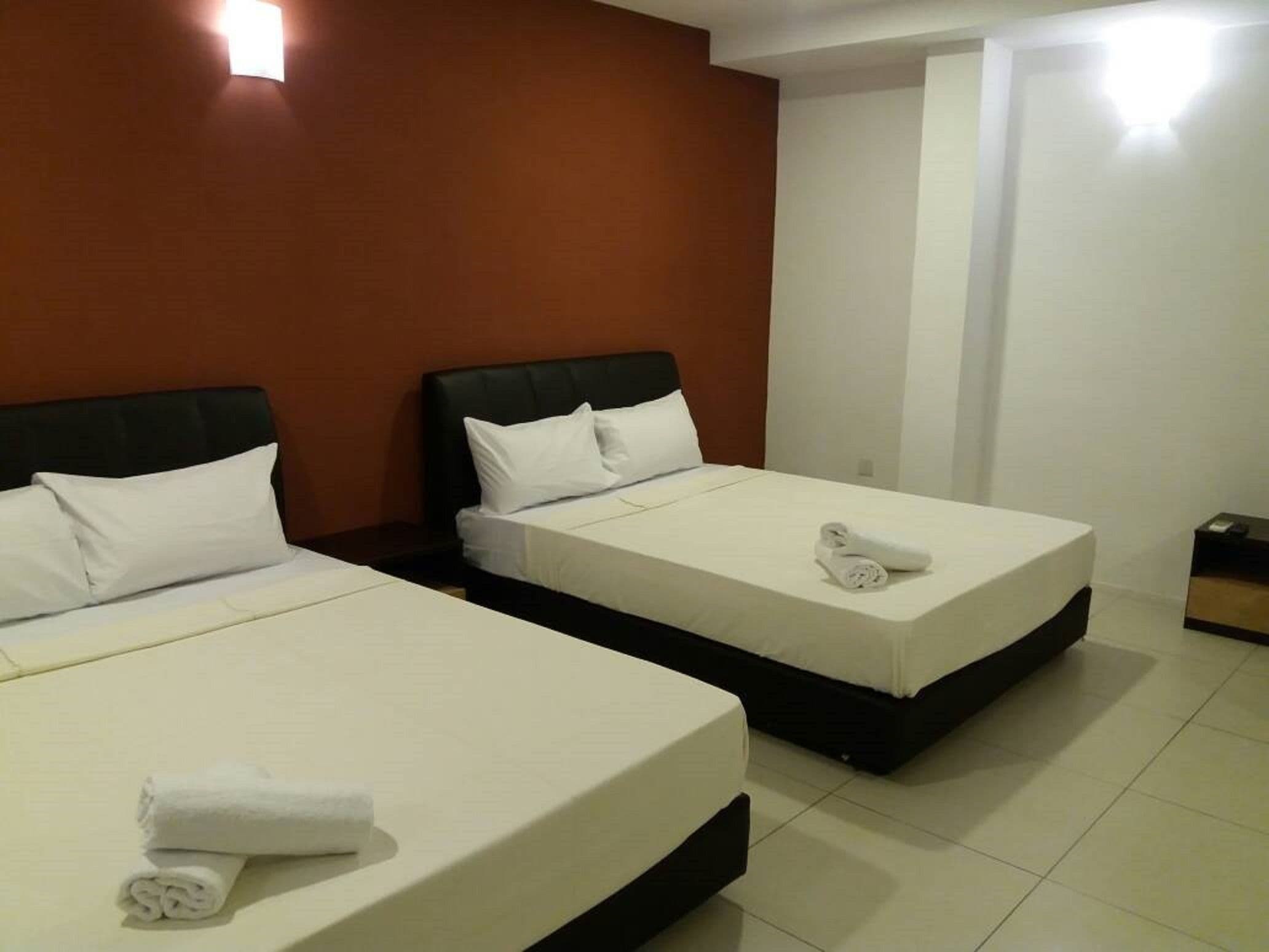 A hotel room with two beds, each with white linens and pillows, and a small bedside table with a towel.