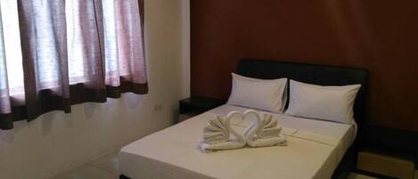 A neatly made bed with white linens and two pillows, a dark headboard, and a wall-mounted light fixture.