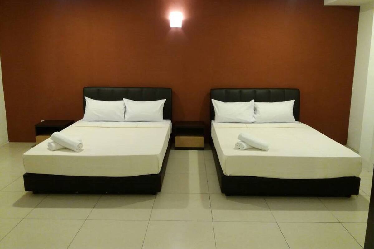 Une chambre d’hôtel avec deux lits, chacun doté de draps et d’oreillers blancs, un mur marron et une petite table de chevet avec une lampe.