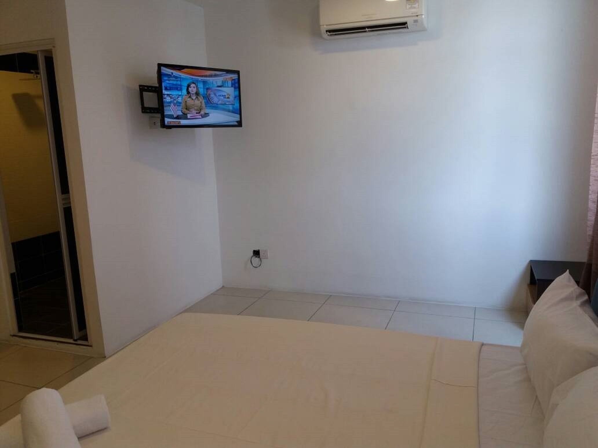 A hotel room with a bed, a television mounted on the wall, and an air conditioning unit.