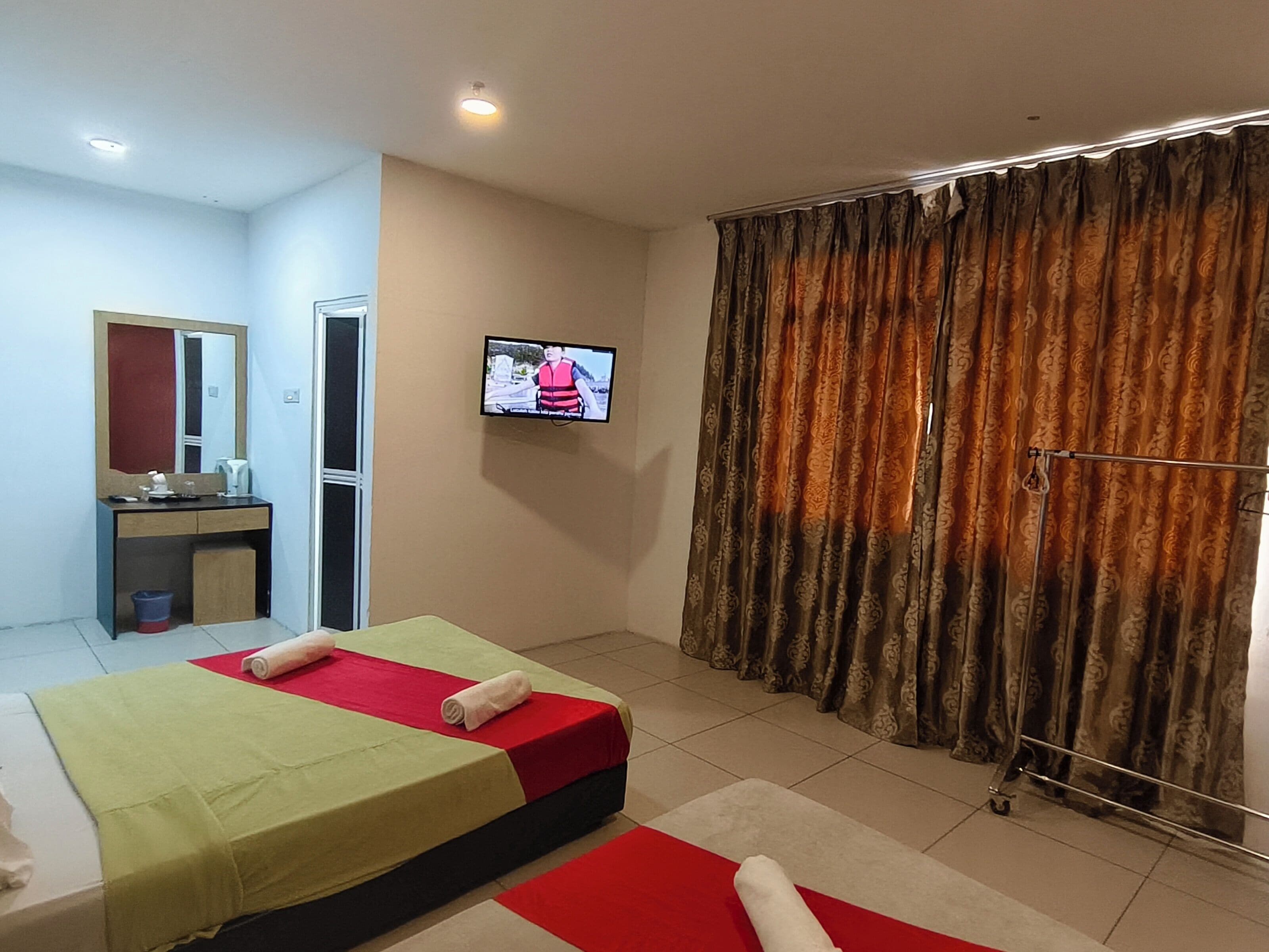 Een hotelkamer met twee bedden, een televisie aan de muur, een badkamer met spiegel en een gordijn.