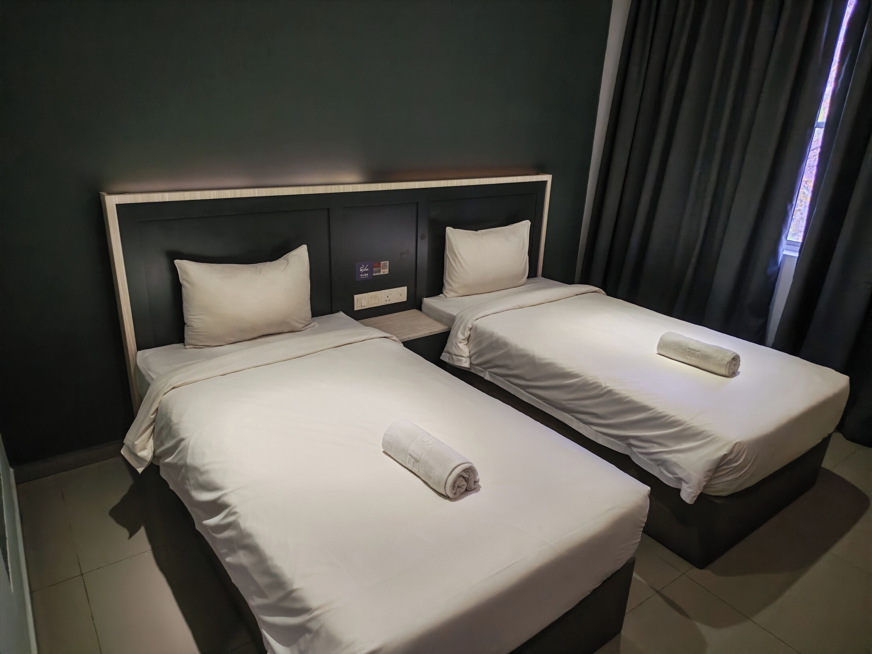 A hotel room with two single beds, each with a pillow and a rolled towel.