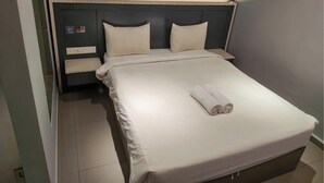 Cama bem arrumada com toalha dobrada, cabeceira e mesa de cabeceira com abajur.