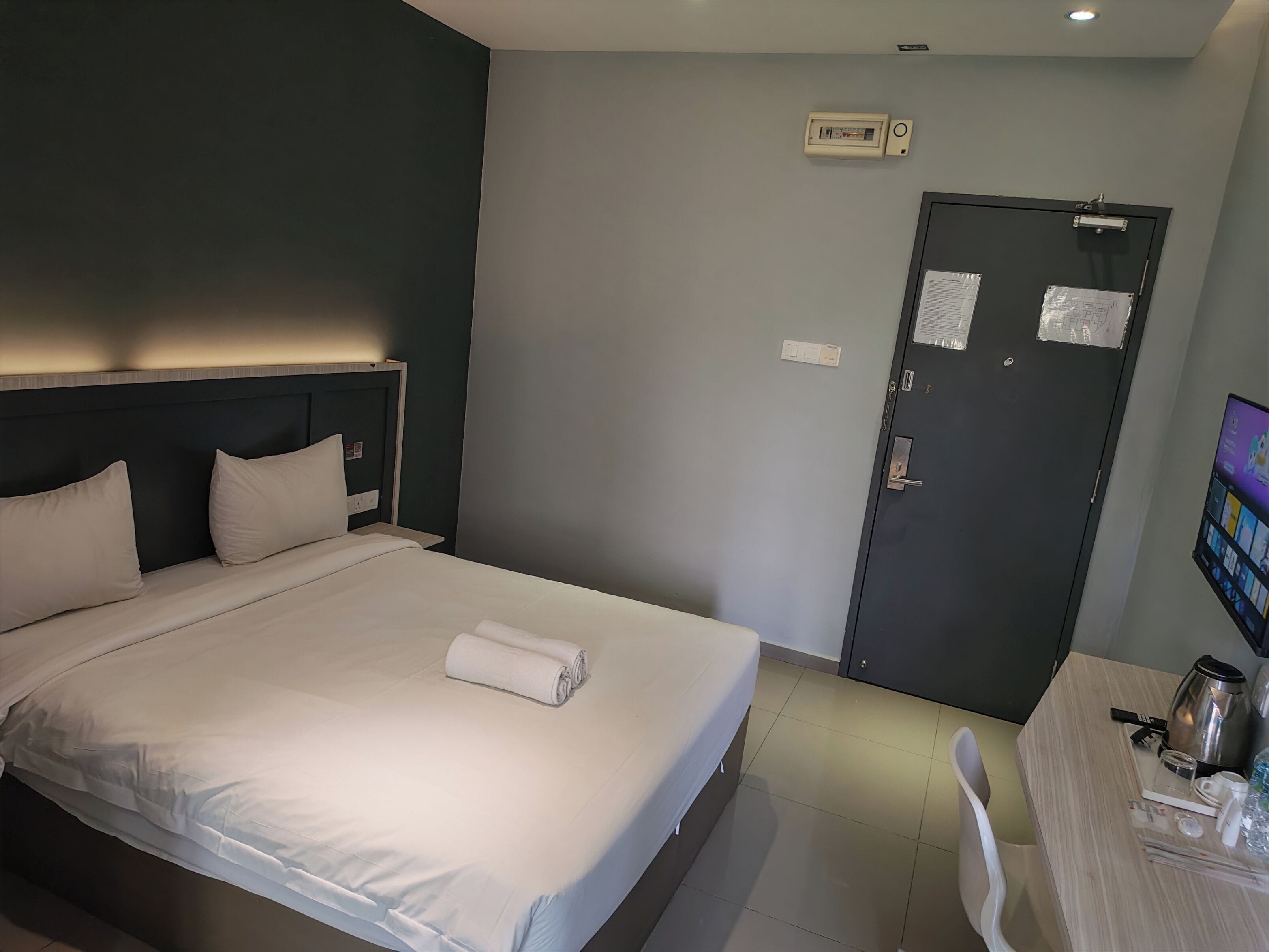 Ein Hotelzimmer mit einem Bett, einem Schreibtisch mit Wasserkocher und einer Tür mit Schloss.
