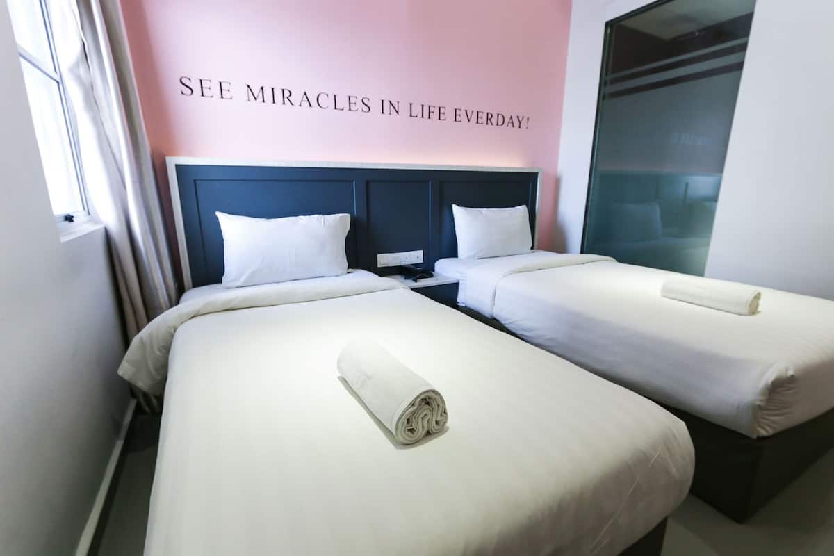 Une chambre d’hôtel avec deux lits, une tête de lit, un mur orné d’une citation inspirante et une fenêtre avec des rideaux.