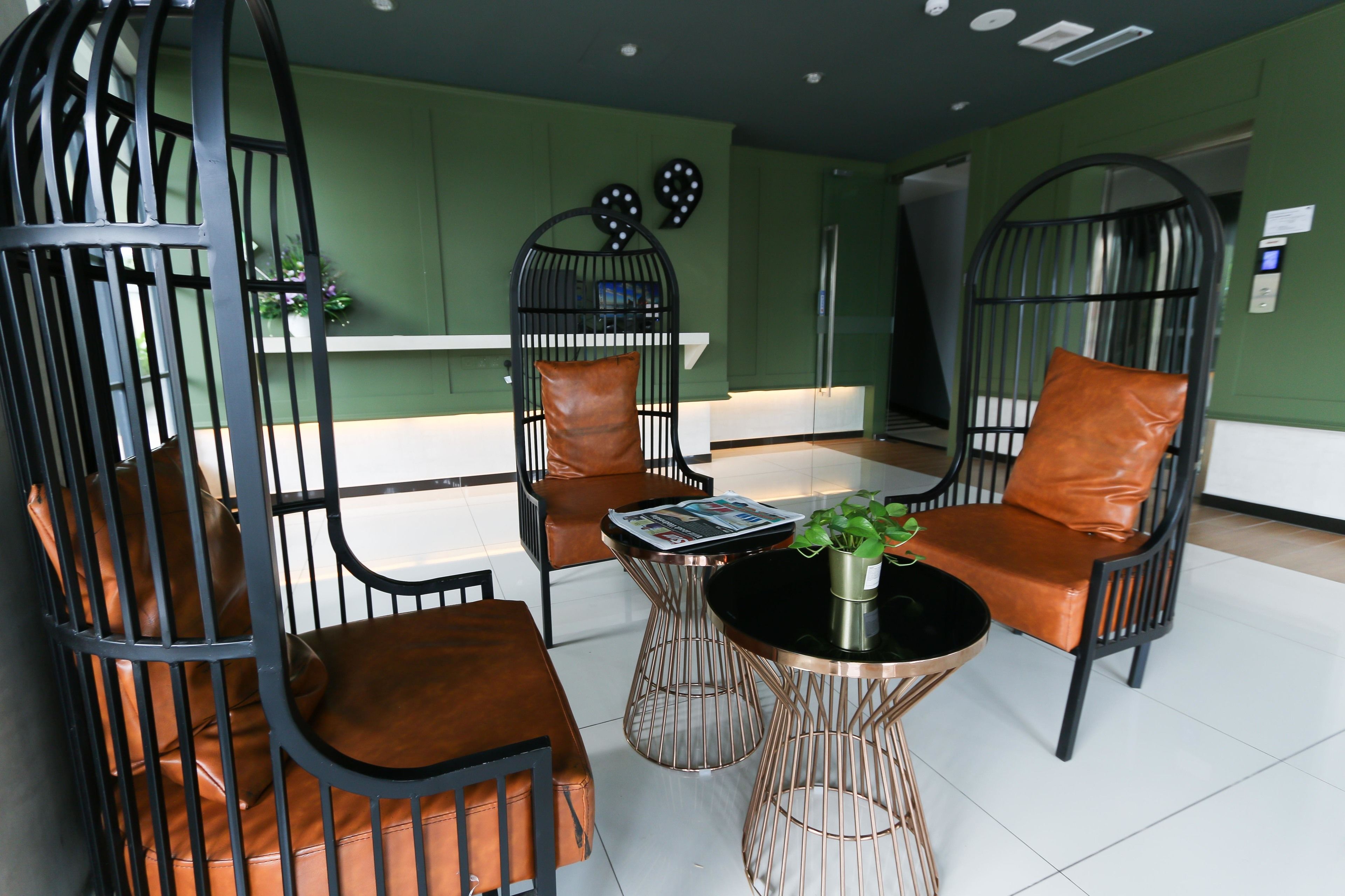 A modern lounge area with metal chairs and a central coffee table, green walls, and a white floor.